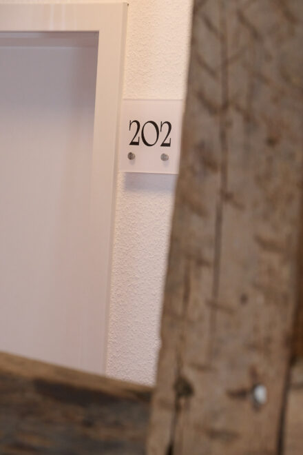 Ein Hotelflur mit Fokus auf das Zimmerschild mit der Aufschrift "202".